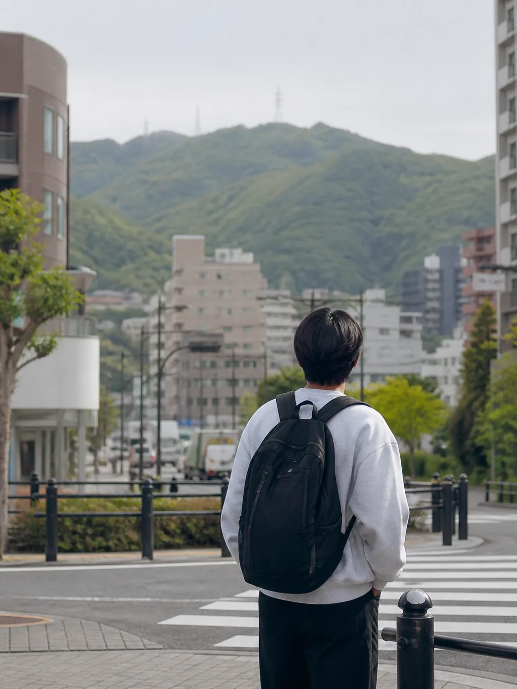 街と緑の山を前に立つ学生と思われる人物の後ろ姿